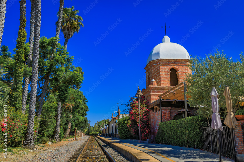 San Juan Capistrano domed bell tower overlooks train tracks framed by palm trees