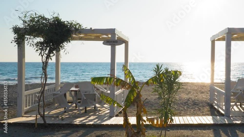 Serene Sunset at Beach Gazebo – Still Shot of White Gazebo and chairs on Sandy Shore with Ocean Backdrop, Golden Hour Tranquility
