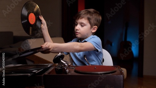 Young boy is choosing a vinyl record to play on a vintage record player. He is concentrating on placing the record carefully on the turntable