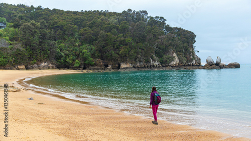 backpacker girl enjoys a walk on the famous beach overlooking split apple rock, unique rock formation in north part of New Zealand South Island near Marahau and Abel Tasman National Park
