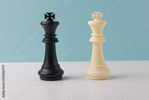 Black and white king chess pieces facing each other on white and light blue background