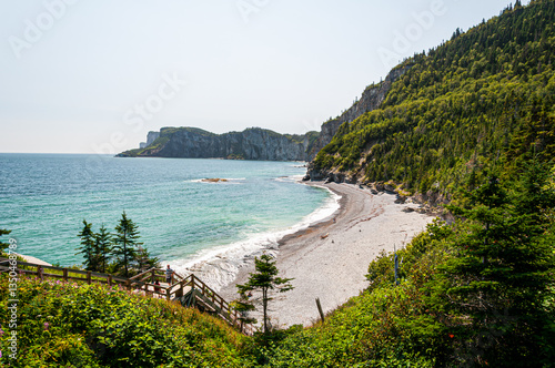 Parc national de ForillonStunning coastal landscape in Gaspésie, Quebec, featuring turquoise waters, a rocky beach, lush green cliffs, and a wooden staircase leading to the shore. A breathtaking natur photo