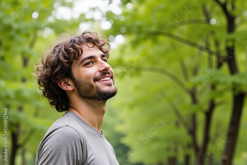 Young Adult Male with Curly Hair Smiling in a Lush Green Park Surrounded by Trees in Daylight