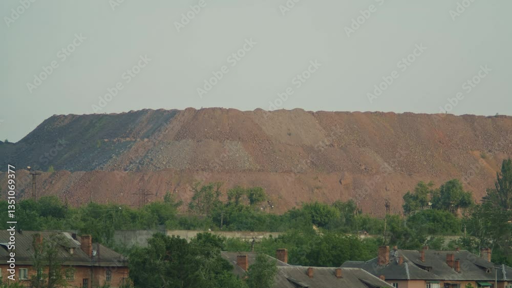Large industrial waste heap or slag heap from mining operations near a residential area with trees and brick houses. Environmental impact and industrial landscape concept. Large industrial waste heap or slag heap from mining operations near a residential area with trees and brick houses. Environmental impact and industrial landscape concept.