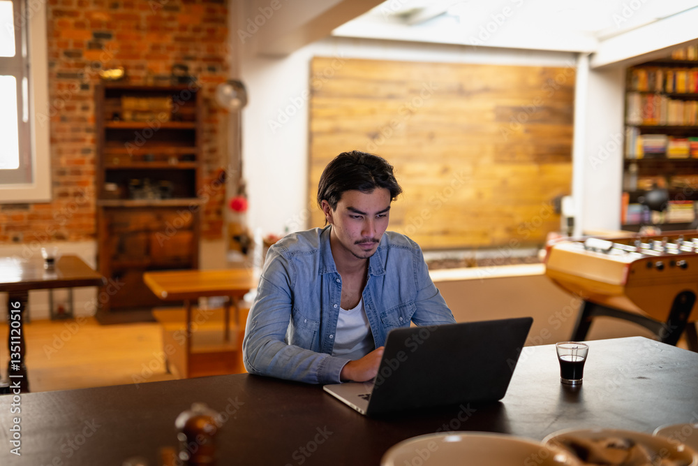 Young man using laptop at home, concentrating on work with coffee nearby Young man using laptop at home, concentrating on work with coffee nearby