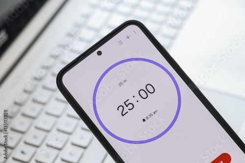 A phone with a black and white 25-minute timer to study with pomodoro method on laptop keyboard, study business background
