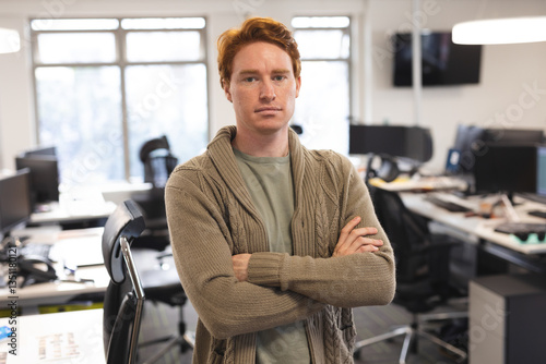 Confident man with red hair standing with arms crossed in modern office photo