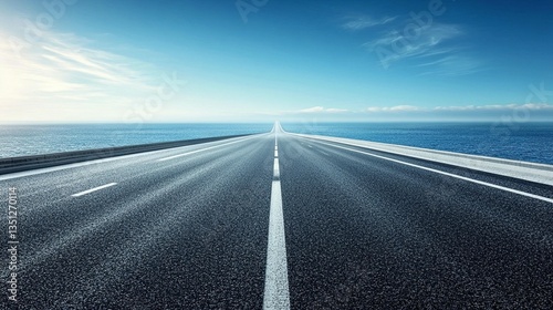 Asphalt road vanishing point over ocean horizon under blue sky.