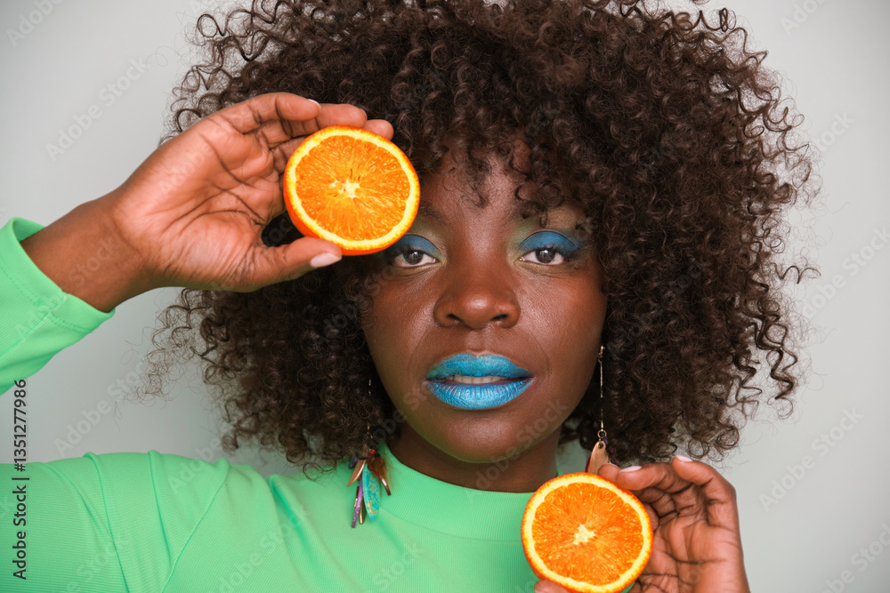 Studio portrait of a young woman with colorful makeup holding orange slices near her eyes