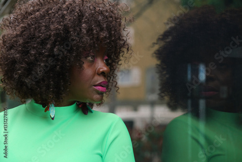 Obraz na płótnie Fashionable black woman with curly hair and colorful earrings looking away and reflecting in a window glass w salonie