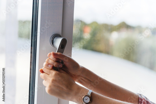 Close-up of hands gripping a modern window handle, indicating difficulty in operation, showcasing the need for ergonomic design and ease of use.