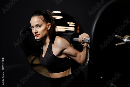 Close-up photo of strong woman doing squats exercises with heavy barbell in the gym