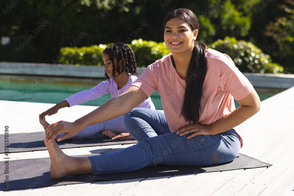 Mother and daughter practicing yoga on mats by pool, enjoying sunny day Mother and daughter practicing yoga on mats by pool, enjoying sunny day
