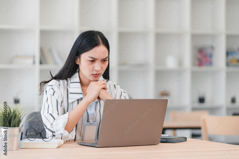Focused Asian businesswoman working on laptop in modern office, expressing determination and concentration. Focused Asian businesswoman working on laptop in modern office, expressing determination and concentration.