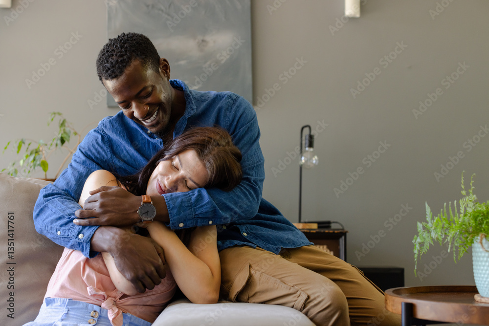 Diverse couple relaxing on couch, embracing and smiling in cozy living room Diverse couple relaxing on couch, embracing and smiling in cozy living room