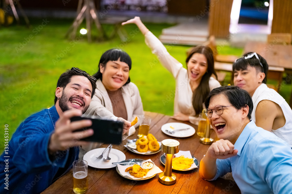 Obraz premium Group of Happy Asian millennial people friends enjoy and fun celebration reunion meeting using mobile phone taking picture together at dinner party in the garden at restaurant on holiday vacation.