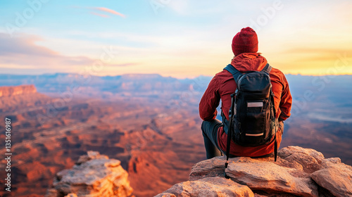 person enjoying breathtaking sunset view from rocky cliff, wearing red beanie and backpack, surrounded by vast landscapes