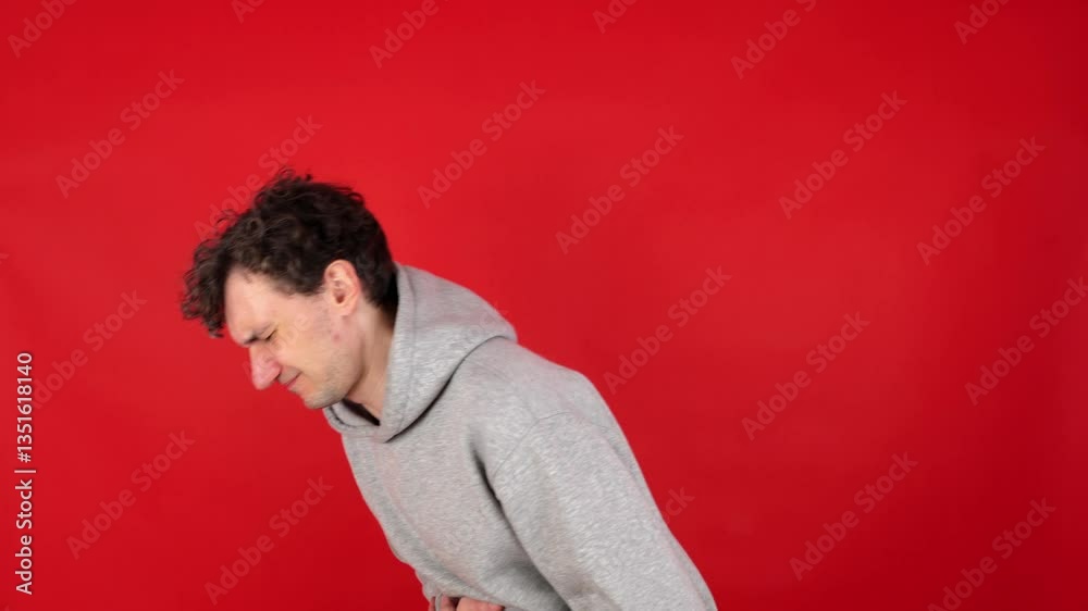 young adult curly man suffers from attacks abdominal pain, stomach, indigestion, poisoning, nausea, heartburn, bloating, colic. Isolated red background, studio shot. concept poor nutrition, fast food young adult curly man suffers from attacks abdominal pain, stomach, indigestion, poisoning, nausea, heartburn, bloating, colic. Isolated red background, studio shot. concept poor nutrition, fast food