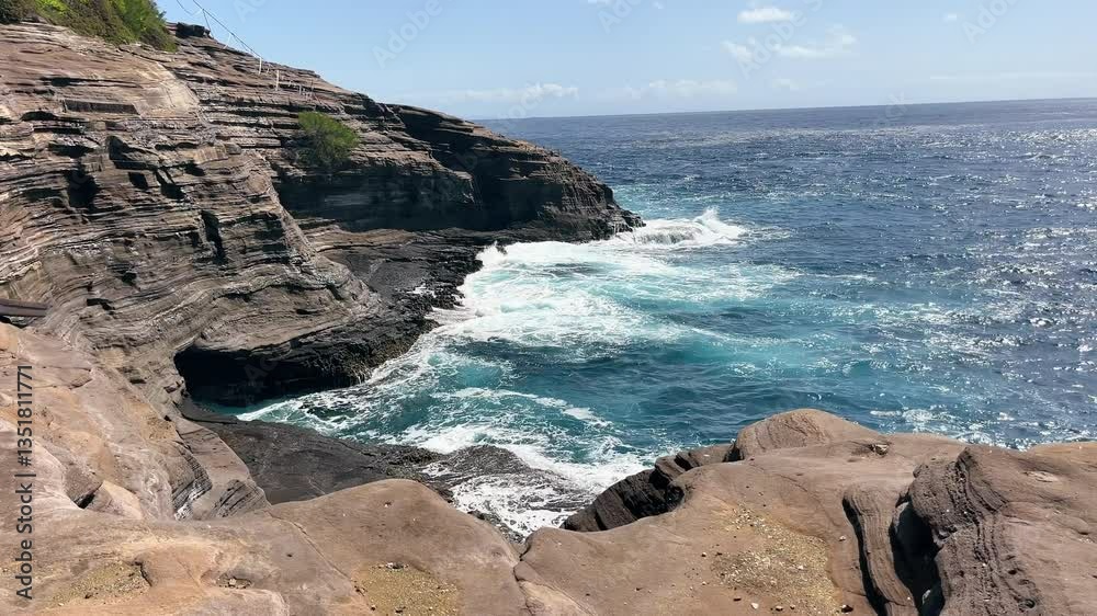 Dramatic volcanic cliffs meet turquoise Pacific Ocean waves along rugged Hawaiian coast under clear sky in bright sunlight Dramatic volcanic cliffs meet turquoise Pacific Ocean waves along rugged Hawaiian coast under clear sky in bright sunlight