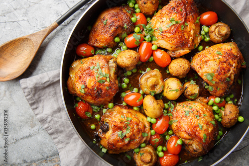 Obraz na płótnie Delicious crispy chicken thighs baked with mushrooms, green peas, cherry tomatoes, garlic and herbs close-up in a frying pan on the table. Horizontal top view from above w salonie