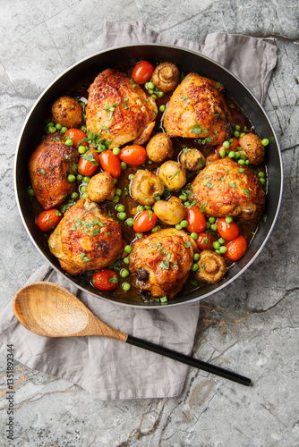 Obraz na płótnie Honey flavored chicken thighs with mushrooms, green peas, cherry tomatoes and herbs close-up in a frying pan on the table. Vertical top view from above w salonie