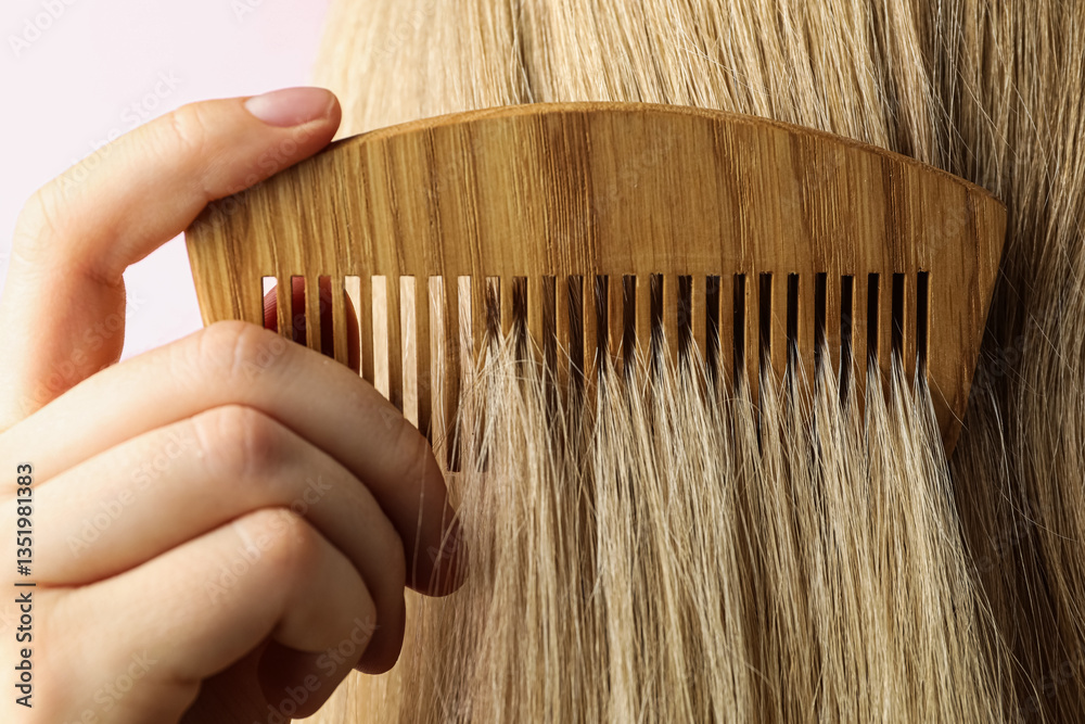 Φωτογραφία Woman brushing hair with wooden comb on pink background, closeup