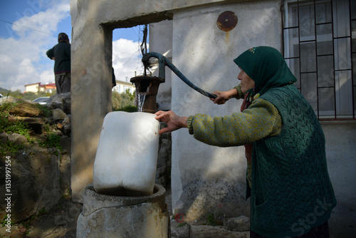 alte Frau füllt Wasser aus Pumpe in Eimer