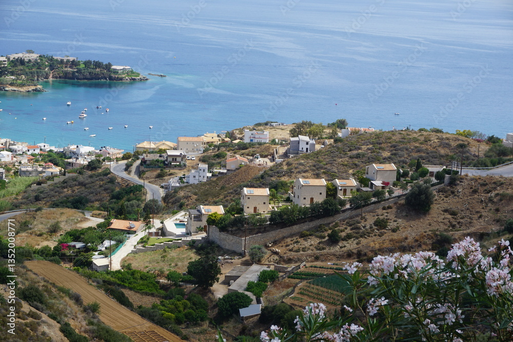 Obraz premium Panoramic view of Agia Pelagia in Crete, Greece from above with the blue sea and the clear blue sky in the background - Holiday homes, villas and hotels with swimming pools amidst beautiful vegetation