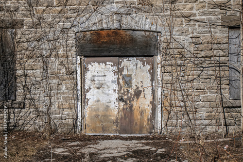 Very old abandoned stone building  overgrown with plants, nobody, wooden door peeling paint, nobody
