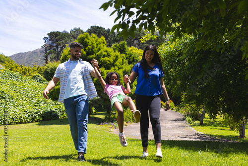 Parents joyfully swinging daughter between them while walking in sunny park