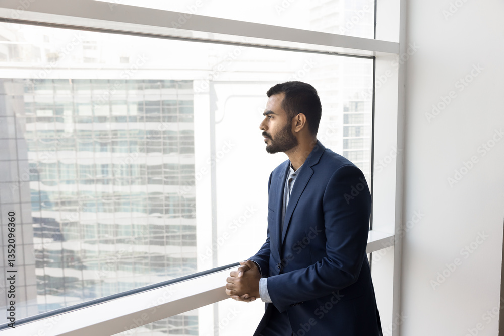 Young 25s thoughtful Indian businessman dressed in suit stands by office window, gazing out city skyline, deep in contemplation or reflection, take break during busy corporate day. Ambition, career Young 25s thoughtful Indian businessman dressed in suit stands by office window, gazing out city skyline, deep in contemplation or reflection, take break during busy corporate day. Ambition, career