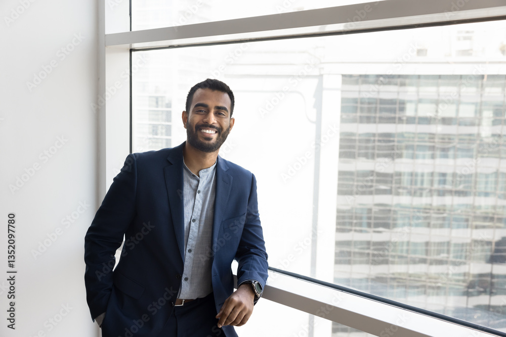 Portrait of confident Indian professional businessman dressed in suit exuding success and positivity, poses by large office window with city view as symbol of ambitions, progress, future opportunities Portrait of confident Indian professional businessman dressed in suit exuding success and positivity, poses by large office window with city view as symbol of ambitions, progress, future opportunities
