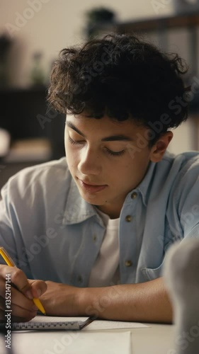 Teenage boy studying at home, preparing for exams and writing in a notebook