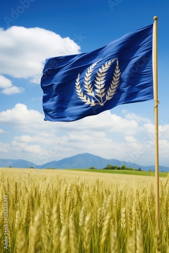 A blue flag with a golden laurel emblem waves proudly in a golden wheat field under a bright blue sky, symbolizing achievement and peace against a picturesque mountainous backdrop