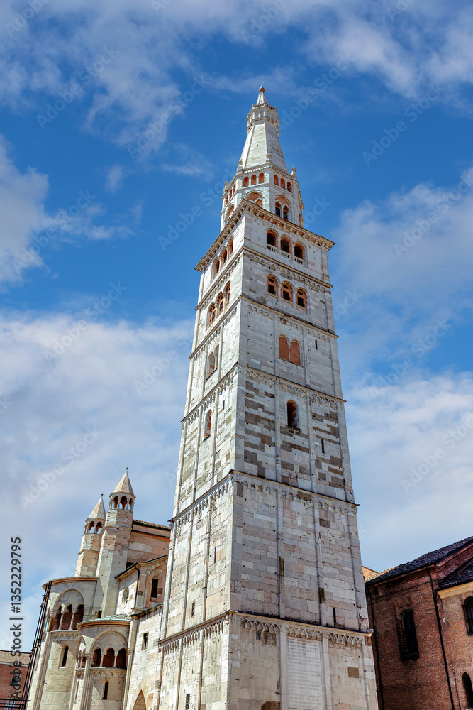 Ghirlandina Tower alongside Modena Cathedral's rear facade. The stunning Cathedral of Modena and Torre Civica tower under a blue sky in Piazza Grande