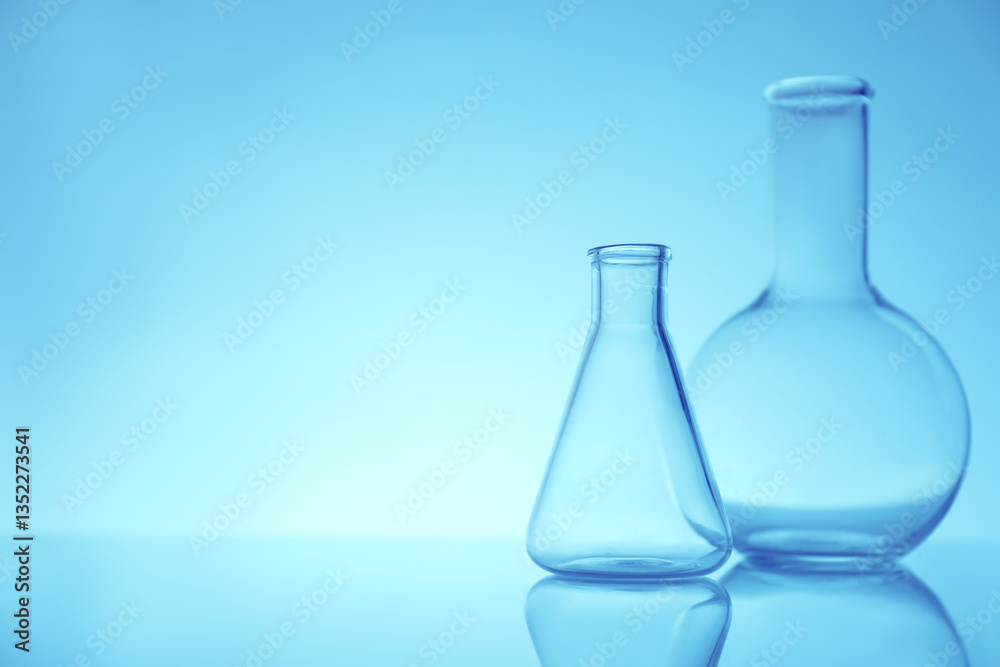 Empty flasks on mirror surface against light blue background, space for text. Laboratory equipment