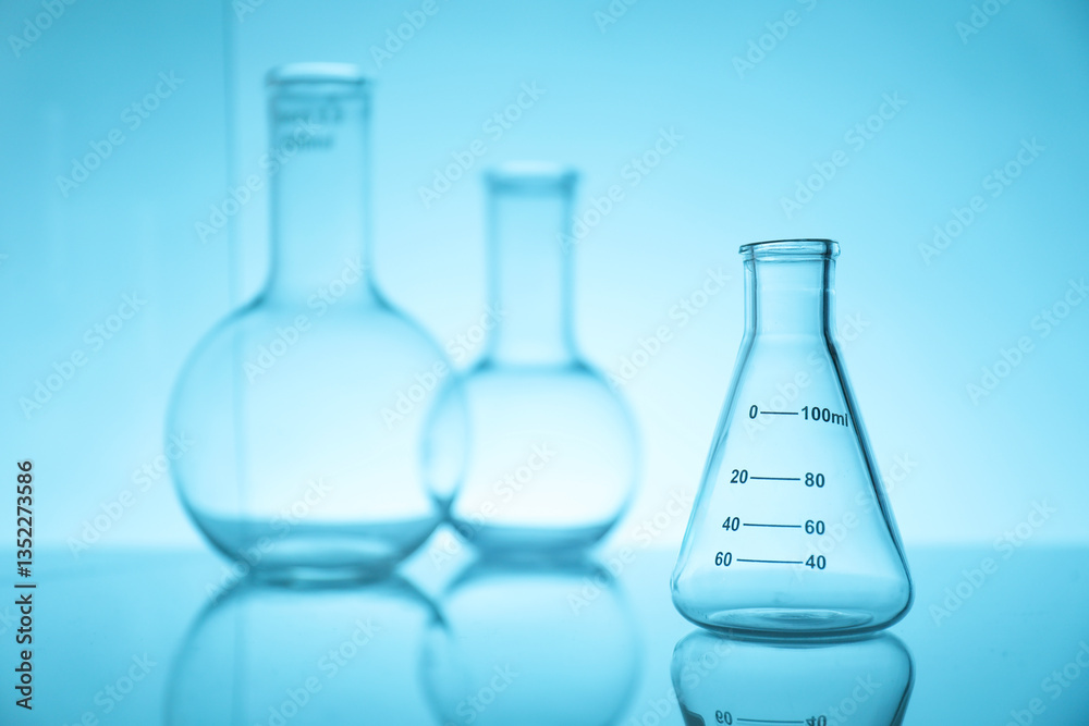 Empty flasks on mirror surface against light blue background. Laboratory equipment Empty flasks on mirror surface against light blue background. Laboratory equipment