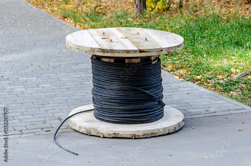 Wooden Spool with Black Cable Outdoors on Sidewalk