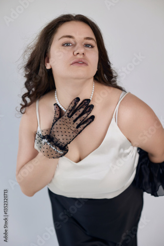Sensual elegant woman in classic black-and-white attire gently touching her neck, with a sheer dotted glove, perfect for stylish editorial content, beauty shoots, and luxury themes.