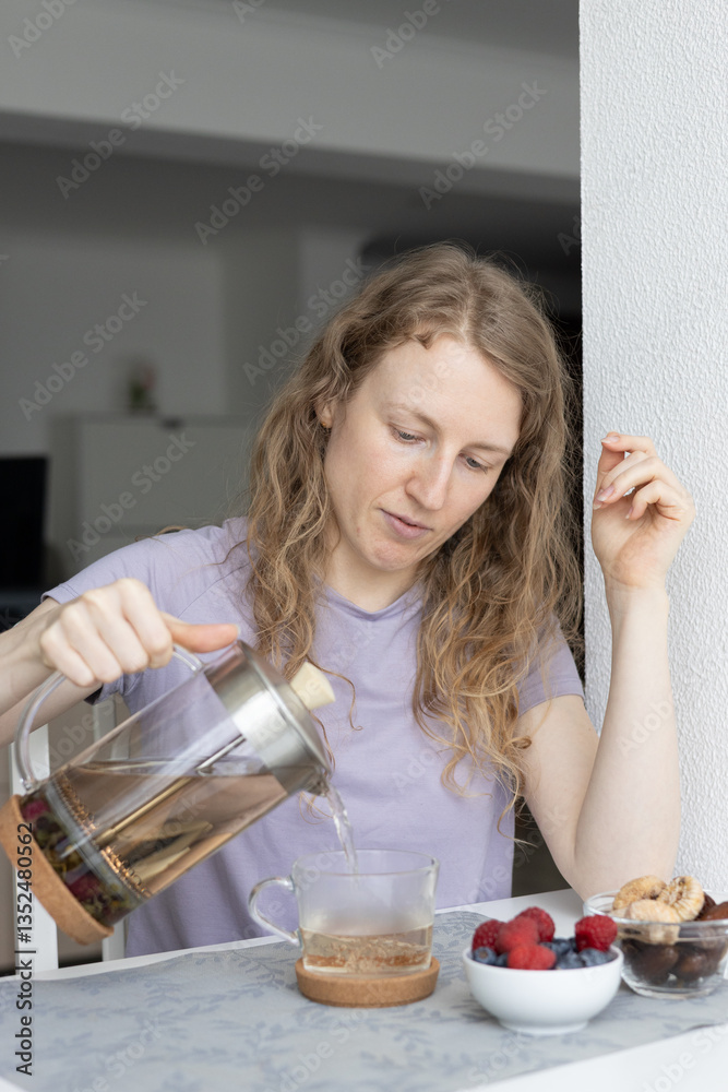 A relaxed woman drinking herbal tea and eating dried fruits and berries at home. Healthy lifestyle and mindful eating concept A relaxed woman drinking herbal tea and eating dried fruits and berries at home. Healthy lifestyle and mindful eating concept