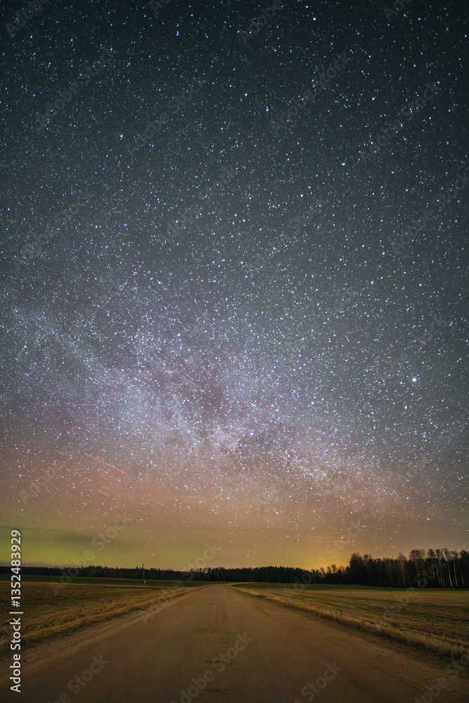Naklejka premium Country road at night with a gorgeous starry sky where the Milky Way is visible on a small northern light