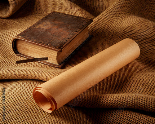 Aged book and rolled parchment rest on brown burlap texture, showcasing a vintage, historical, or literary concept, ideal for antique or scholarly themes