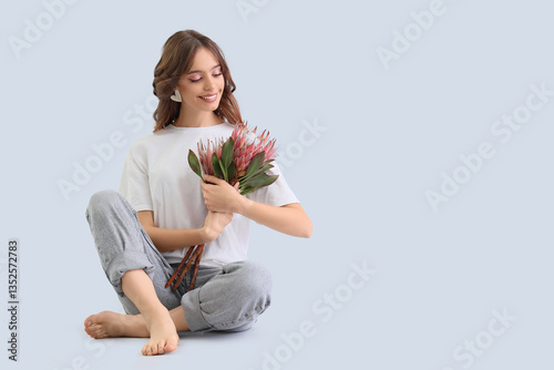 Young woman with protea flowers sitting on light background