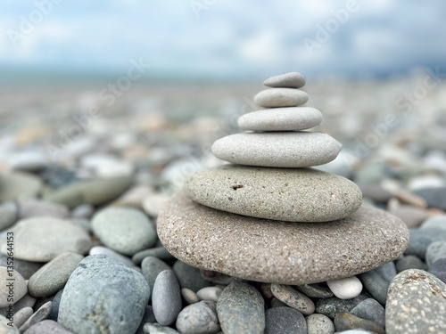 Stacked pebbles on pebbly beach with ocean background. Closeup of balanced pyramid stone stack on beach with sea view. Zen rock. Meditation, mindfulness and tranquility concept