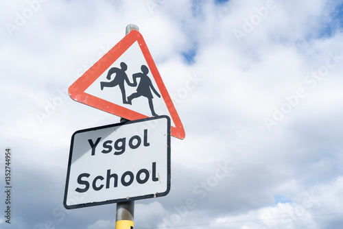 Roadsigns with the symbol for children and the words 'school' in English and Welsh against a cloudy sky.