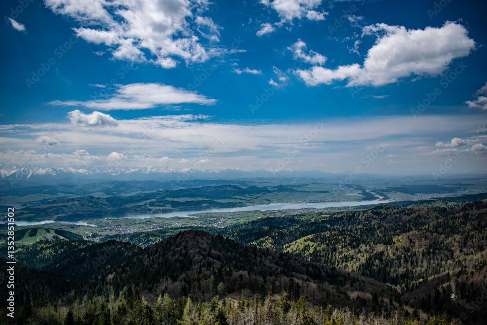 green mountains and valleys. In the background, rocky snow-capped mountains are visible green mountains and valleys. In the background, rocky snow-capped mountains are visible