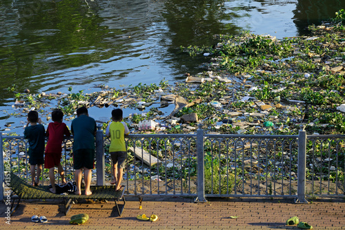 Children looks on the big amount of trash polluting the water of Saigon river in Ho Chi Minh City, Vietnam.