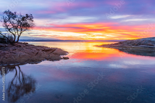 A vibrant sunset reflected in still water between two rocky points