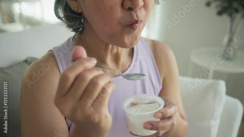 Asia adult people middle age happy old woman eat greek yogurt cup weight loss protein gut health care diet detox sit at home sofa elder aging asian aged female. Fresh medical food relief meal enjoy.