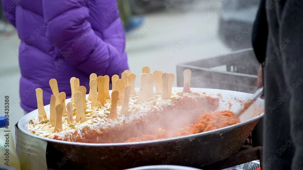 Street food vendor cooking stirring steaming Gajar ka Halwa carrot cake sweet dessert with wooden spoons placed on it a common festiival dish during Eid, Diwali, Holi in north India